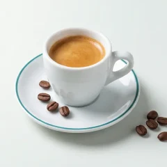 فنجان اسپرسو با کرمای قهوه‌ای روی نعلبکی و چند دانهٔ قهوه